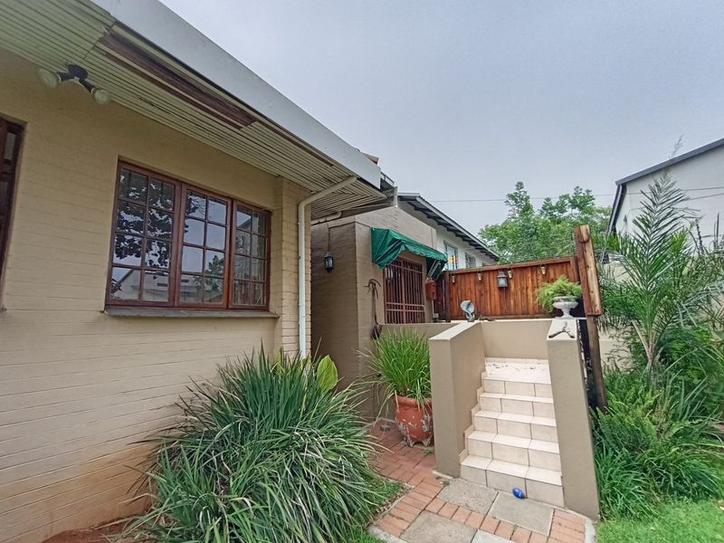 Rear exterior view of the house featuring brick facade, timber window frames, and a tiled staircase leading to a raised outdoor area.