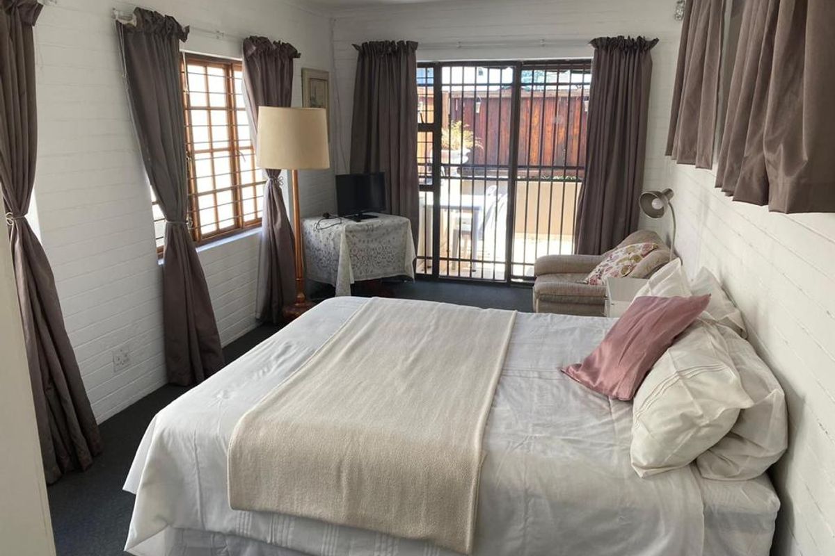 A bedroom featuring painted brick walls, timber-framed windows, and a sliding security gate providing access to the outdoor area.