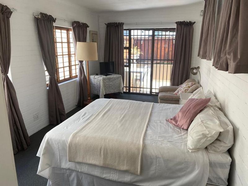 A bedroom featuring painted brick walls, timber-framed windows, and a sliding security gate providing access to the outdoor area.