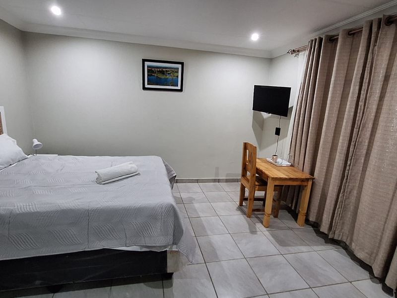 A functional bedroom featuring neutral wall tones, tiled flooring, and recessed lighting, providing a clean and simple living space.