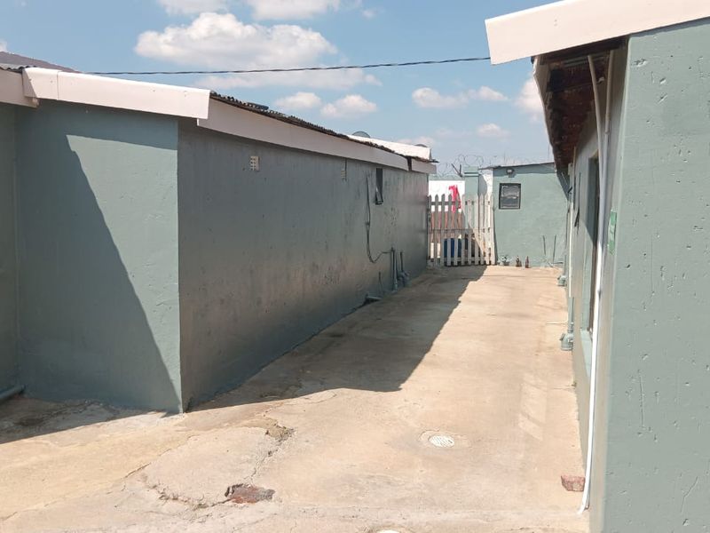A narrow exterior rear passage featuring concrete paving, perimeter walls, and a security gate, showing signs of wear and weathering.