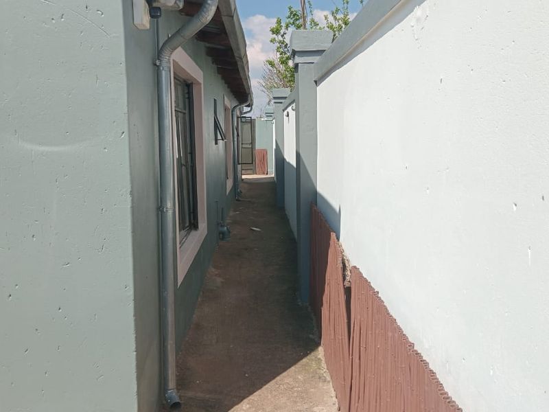 A narrow side passage between the house exterior and the boundary wall, featuring concrete paving and drainage downpipes.