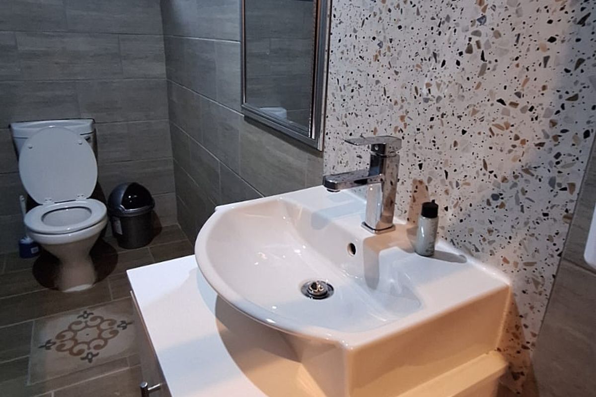 A modern bathroom featuring a vessel sink on a white vanity cabinet, terrazzo accent wall tiling, and a standard toilet.