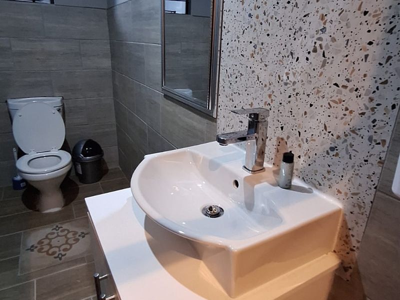 A modern bathroom featuring a vessel sink on a white vanity cabinet, terrazzo accent wall tiling, and a standard toilet.