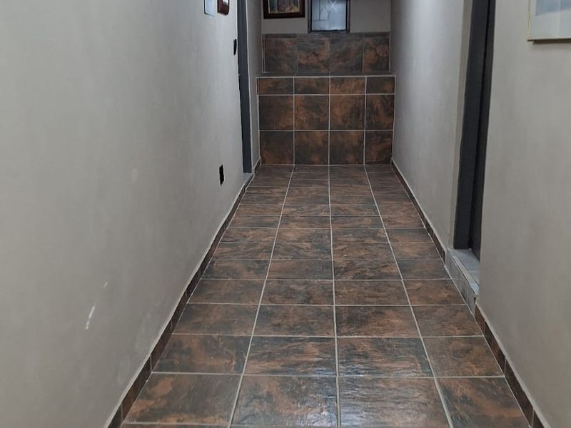 A long hallway featuring dark ceramic floor tiles, recessed lighting, and a ceiling access hatch. The space requires minor maintenance and cosmetic updates.
