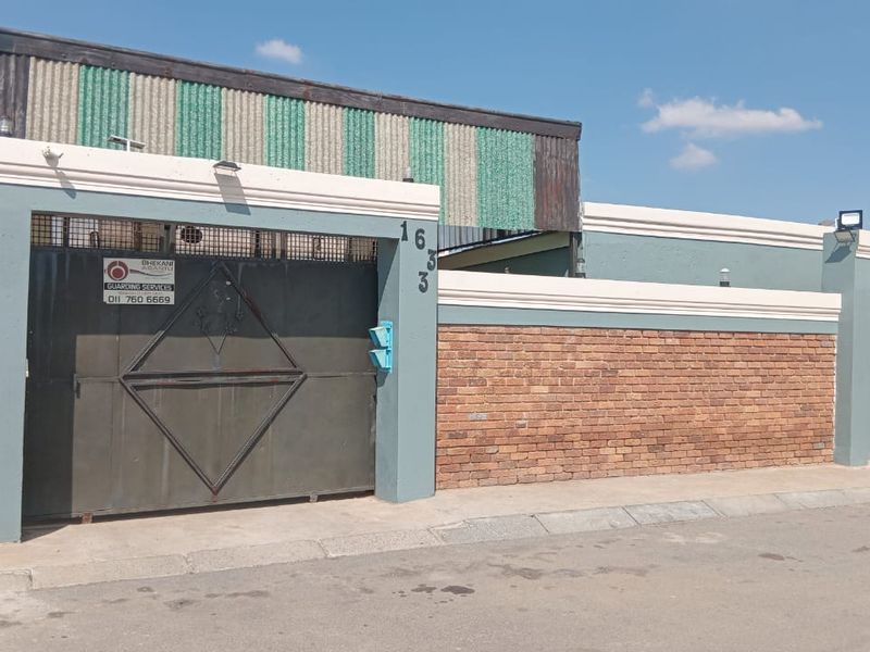 Front elevation of the property featuring a brick boundary wall, secure metal gate, and corrugated metal roofing.