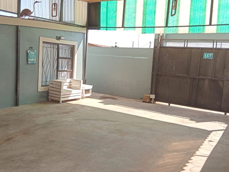 A spacious, covered garage area featuring concrete flooring, secure metal gate access, and protective security bars on the window.