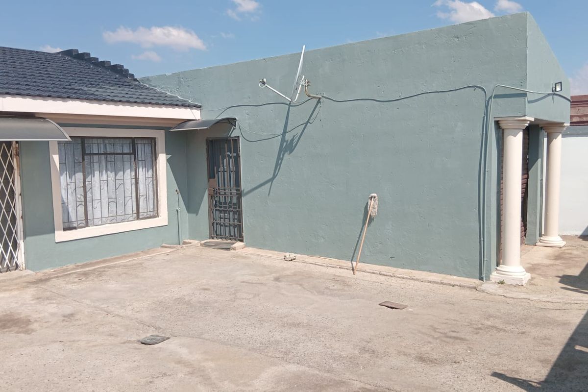 Rear exterior view of the property featuring a concrete patio area, security gates, and structural columns.