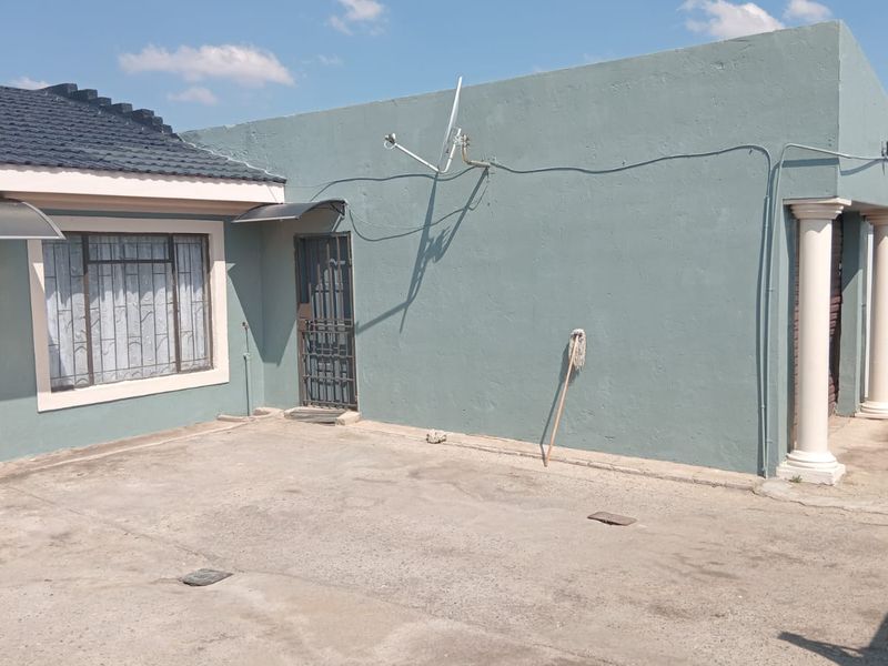 Rear exterior view of the property featuring a concrete patio area, security gates, and structural columns.