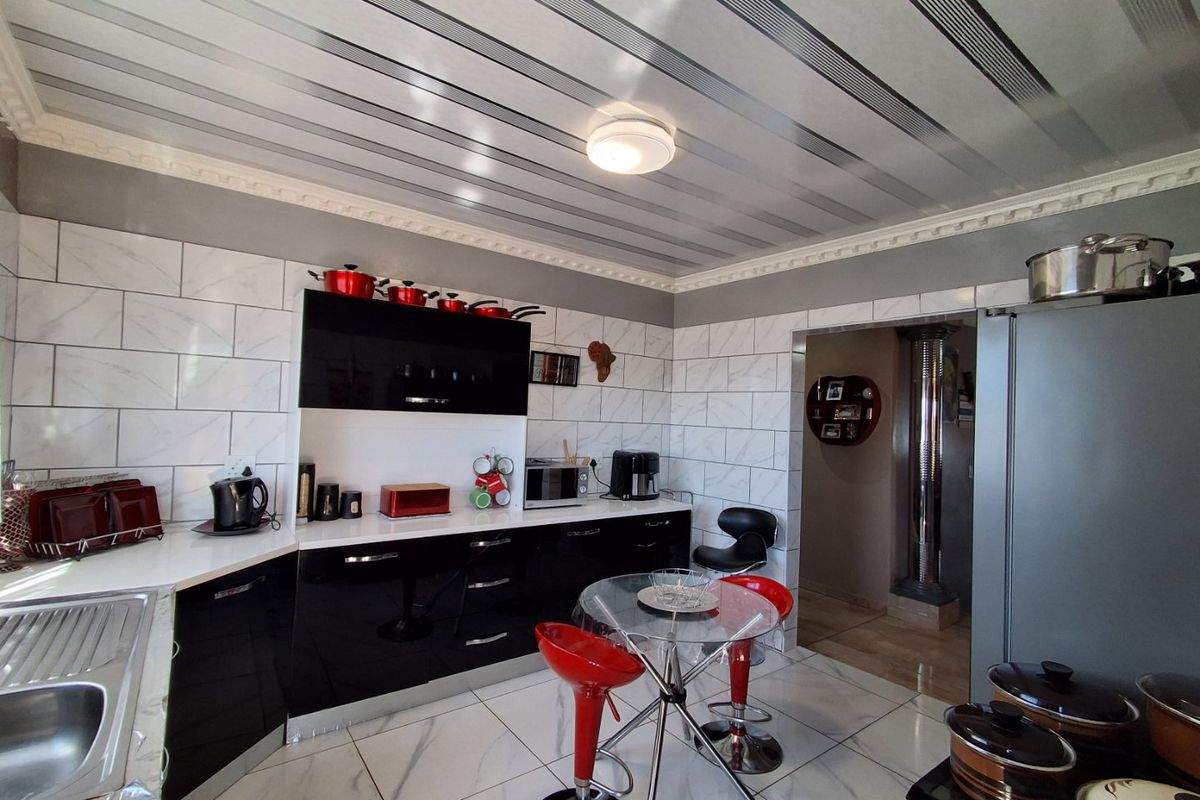 Modern kitchen featuring high-gloss black cabinetry, marble-effect wall and floor tiling, and decorative ceiling panels with integrated lighting.