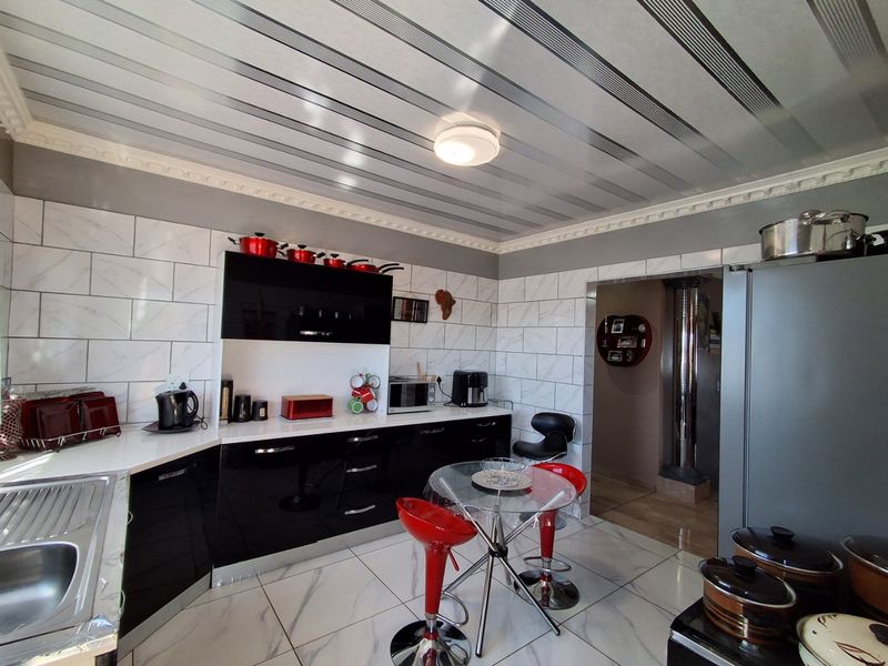 Modern kitchen featuring high-gloss black cabinetry, marble-effect wall and floor tiling, and decorative ceiling panels with integrated lighting.