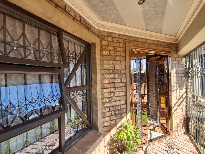 Covered patio area featuring face brick walls, secure aluminium window frames, and decorative ceiling cornicing, providing a functional outdoor transition space.
