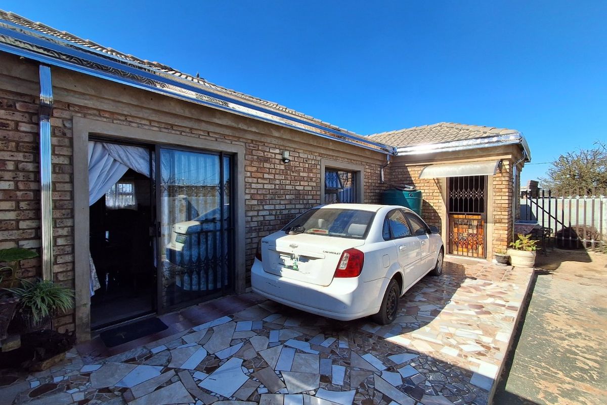 Rear exterior view of a brick house featuring a paved patio area, sliding glass doors, and a security gate entrance.