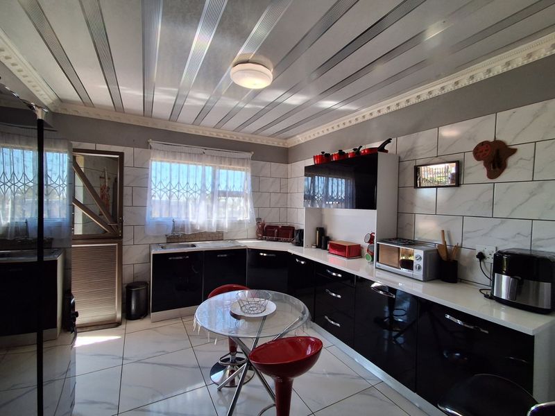 Modern kitchen featuring high-gloss black cabinetry, marble-effect wall tiling, tiled flooring, and a unique panelled ceiling design.