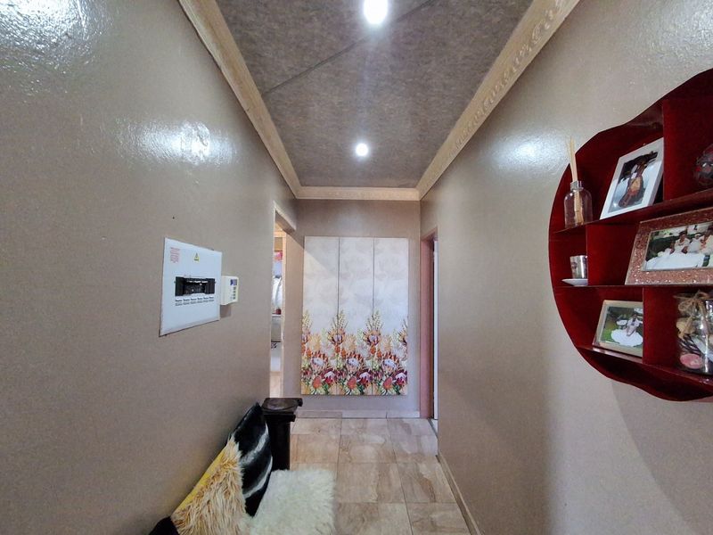 A well-lit hallway featuring tiled flooring, a recessed ceiling with decorative cornice, and a wall-mounted electrical distribution board.