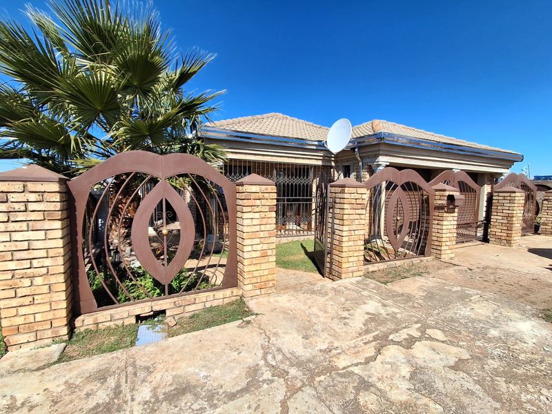 Front exterior view of a single-story house featuring a brick boundary wall, decorative metal gates, and a tiled roof with a paved driveway.