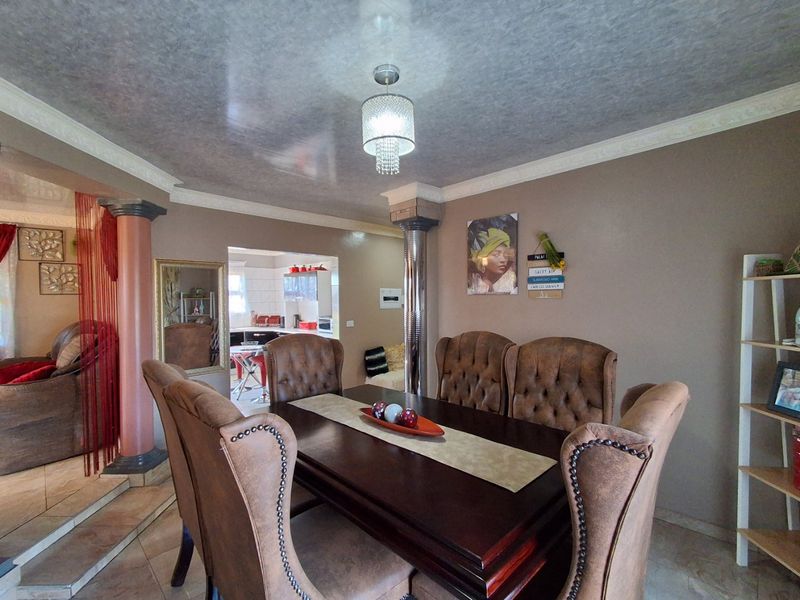 A formal dining room featuring decorative columns, crown molding, and tiled flooring, with an open-plan view into the adjacent kitchen area.