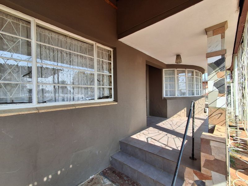 A covered front porch entrance featuring tiled steps, a metal handrail, and decorative tiled pillar cladding with security bars on the windows.