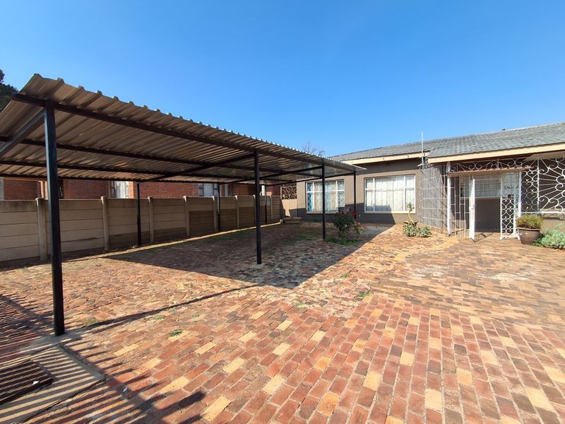 Rear exterior area featuring a large metal carport, extensive brick paving, and secure access to the main house.