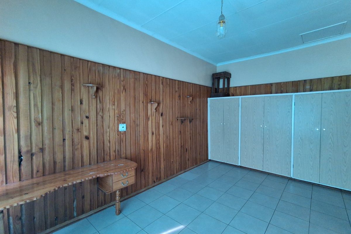A spacious bedroom featuring timber wall paneling, built-in cupboards, a fixed desk, and tiled flooring, offering a blank canvas for renovation.