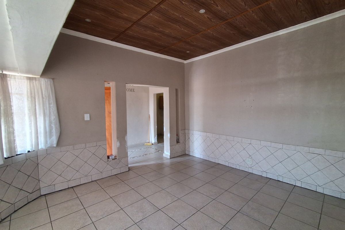 An empty living area featuring tiled flooring, decorative wall tiling, and a wood-look ceiling, currently requiring finishing touches to the wall plastering.