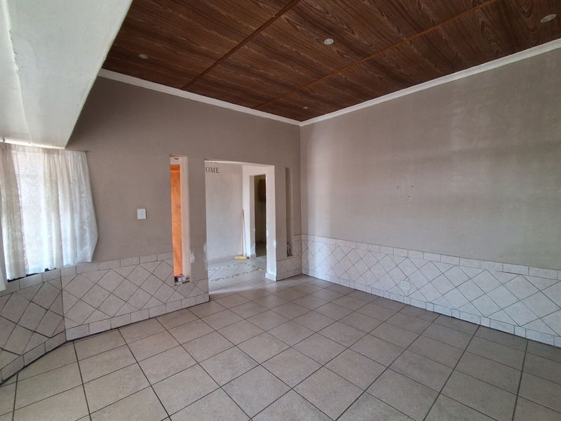 An empty living area featuring tiled flooring, decorative wall tiling, and a wood-look ceiling, currently requiring finishing touches to the wall plastering.
