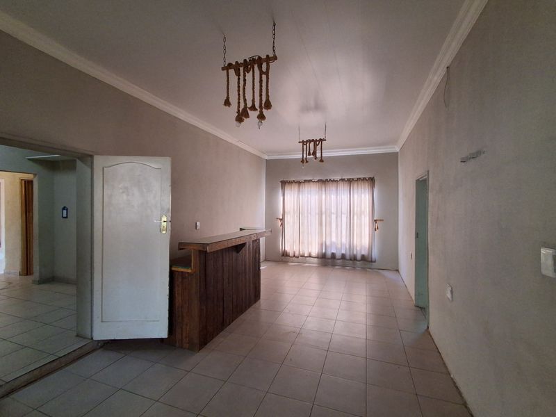 An empty room featuring a built-in wooden bar counter, tiled flooring, and decorative pendant lighting, offering a versatile space for entertainment.