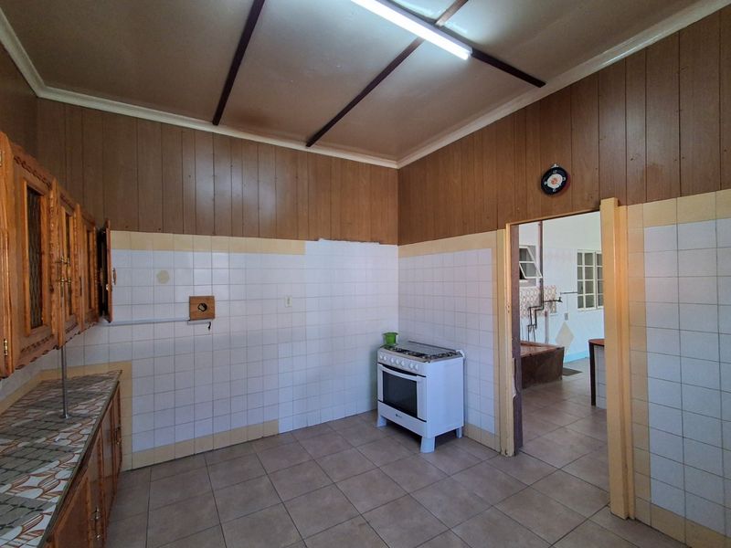 A dated kitchen featuring wooden wall paneling, tiled splashbacks, and tiled flooring, with a freestanding stove and built-in cabinetry.