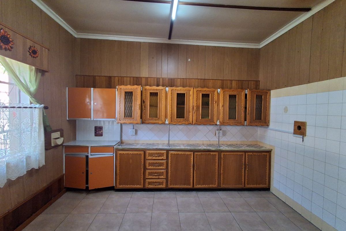 A spacious kitchen featuring dated wooden cabinetry, tiled backsplash, and tiled flooring, offering a blank canvas for modern renovation and design updates.