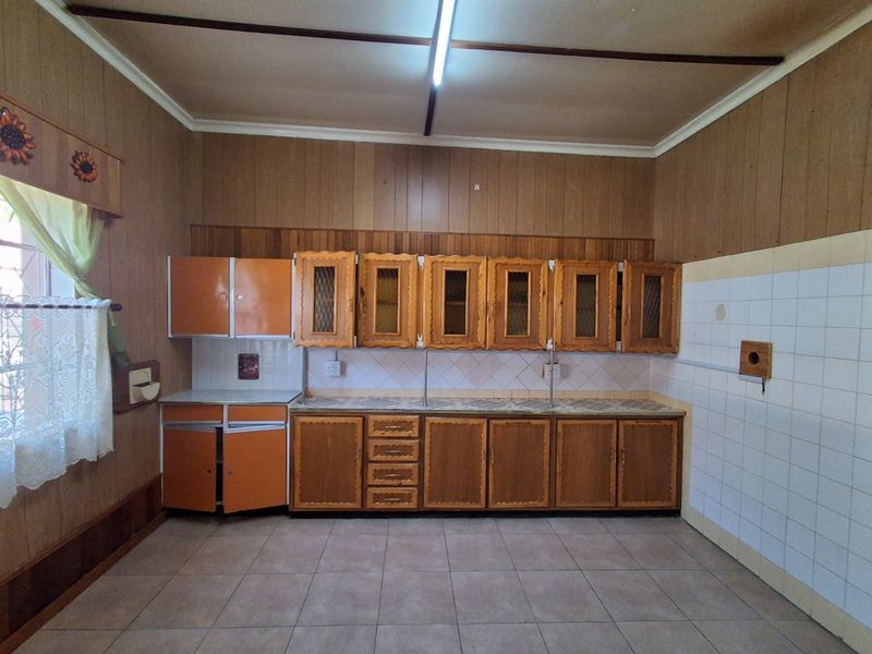 A spacious kitchen featuring dated wooden cabinetry, tiled backsplash, and tiled flooring, offering a blank canvas for modern renovation and design updates.