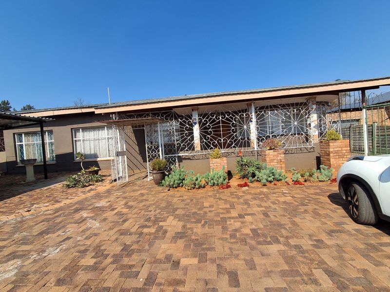 Front exterior view of a single-story house featuring a brick paved driveway, covered patio area, and decorative wrought iron security screening.