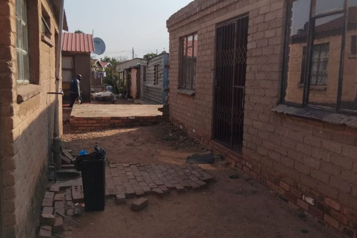 Rear exterior view of a brick residential property showing a narrow courtyard area with basic paving and security gate access.