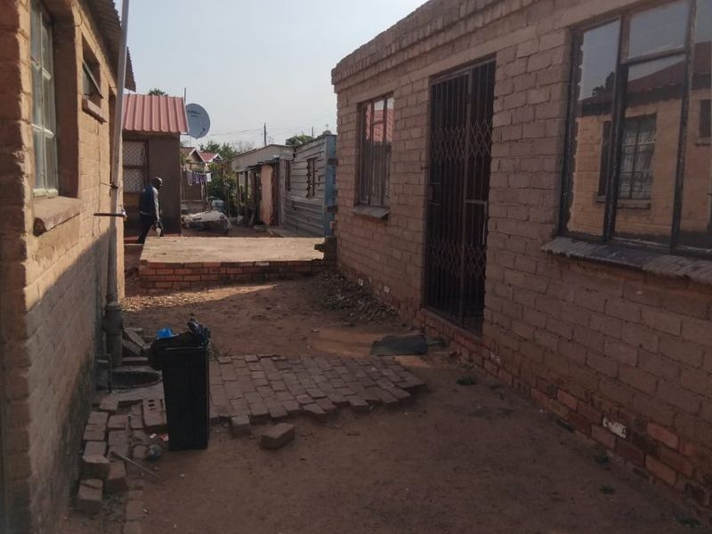 Rear exterior view of a brick residential property showing a narrow courtyard area with basic paving and security gate access.