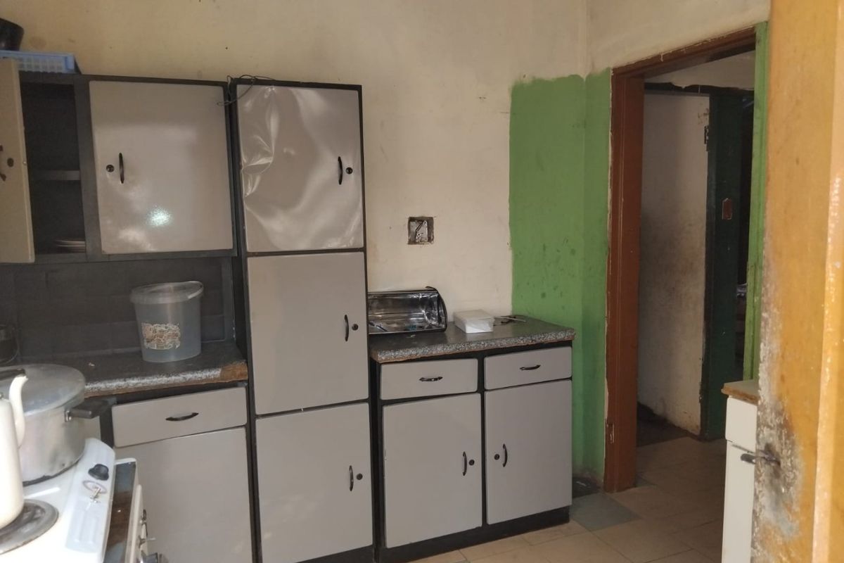A dated kitchen featuring built-in cabinetry, laminate countertops, and tiled flooring, requiring cosmetic updates and repairs to the wall finishes and cabinet doors.