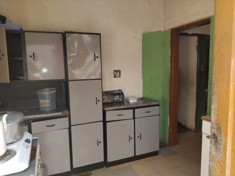 A dated kitchen featuring built-in cabinetry, laminate countertops, and tiled flooring, requiring cosmetic updates and repairs to the wall finishes and cabinet doors.