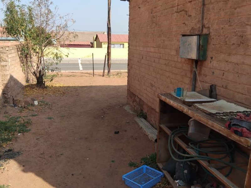 A view of the rear exterior area featuring exposed brick walling and an external electrical distribution box on an unpaved yard.