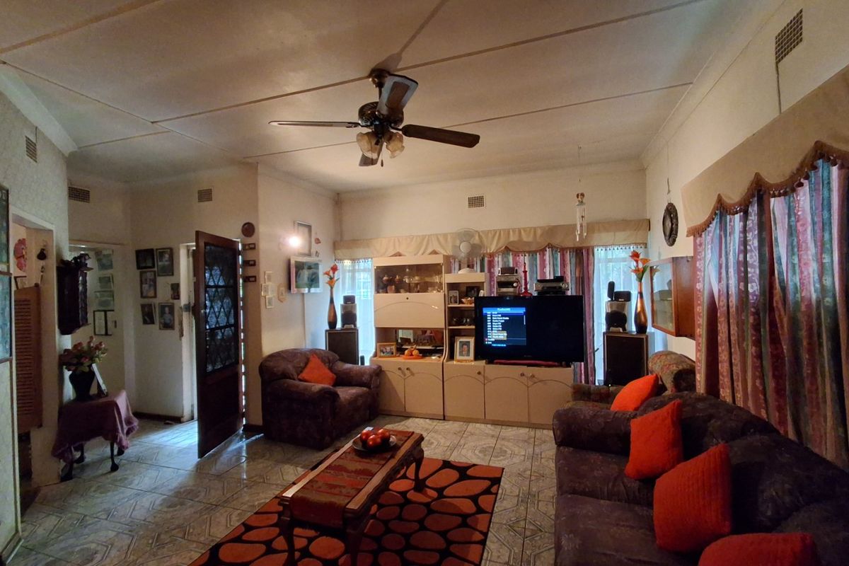 A living room featuring tiled flooring, a ceiling fan, and built-in cabinetry, showing signs of wear and dated finishes.