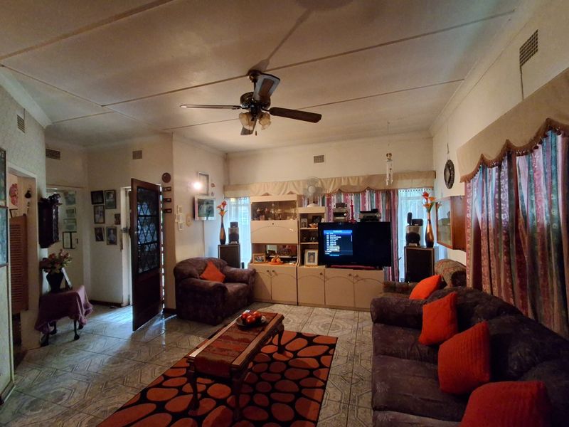 A living room featuring tiled flooring, a ceiling fan, and built-in cabinetry, showing signs of wear and dated finishes.