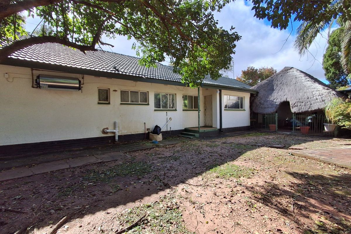 Rear view of the property featuring a tiled roof, solar water heater, and a detached thatched lapa area set within a large garden space.