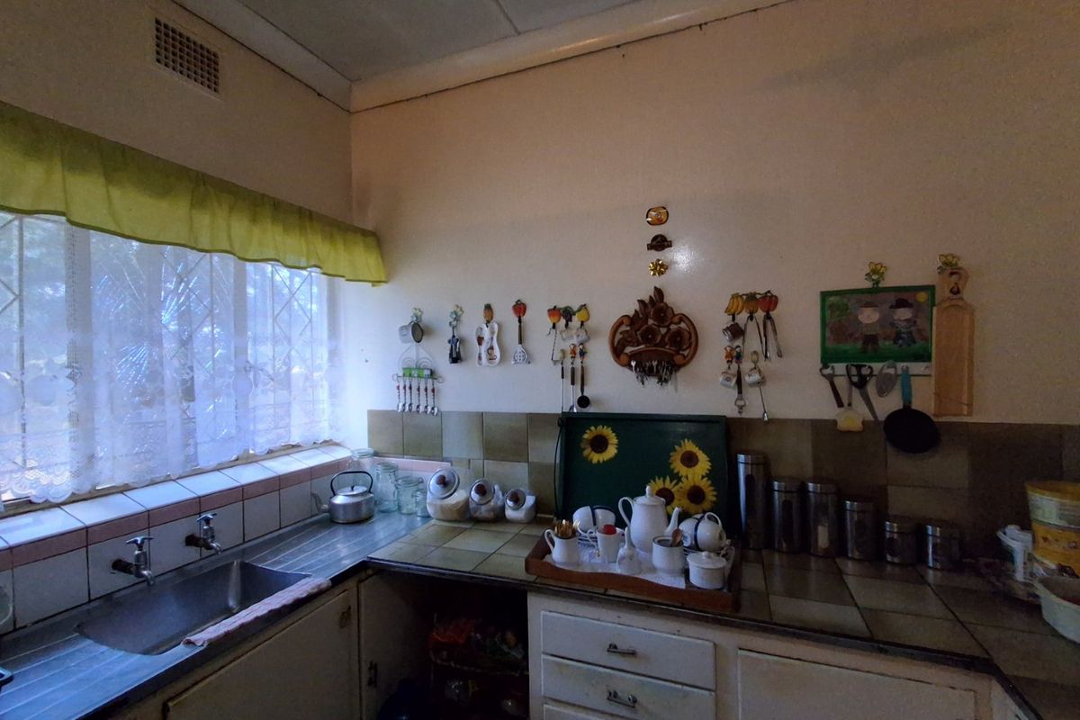 A dated kitchen featuring original tiled countertops, a stainless steel sink, and built-in cabinetry, offering significant potential for a modern renovation.