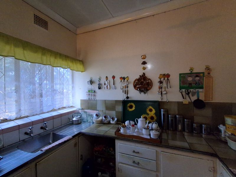 A dated kitchen featuring original tiled countertops, a stainless steel sink, and built-in cabinetry, offering significant potential for a modern renovation.