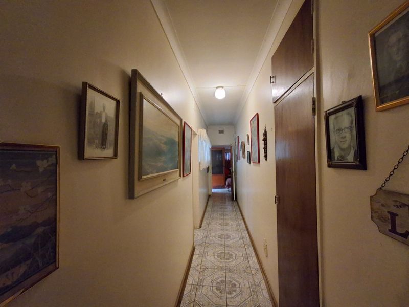 A functional residential hallway featuring tiled flooring and a built-in storage cupboard, providing access to various rooms within the home.