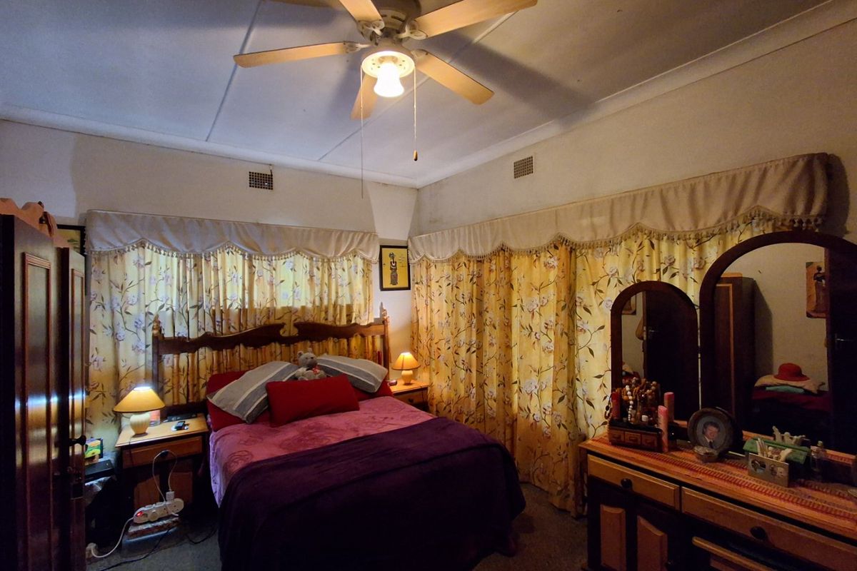 A bedroom featuring a ceiling fan and ventilation grilles, showing signs of dated finishes and wall discoloration.