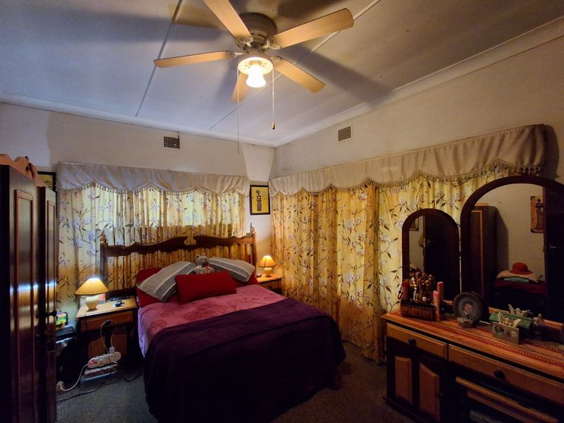 A bedroom featuring a ceiling fan and ventilation grilles, showing signs of dated finishes and wall discoloration.