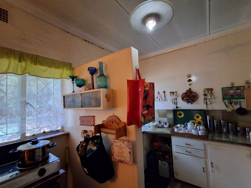 A dated kitchen area featuring built-in cabinetry, a tiled backsplash, and a window with security bars, requiring cosmetic updates to modernize the space.