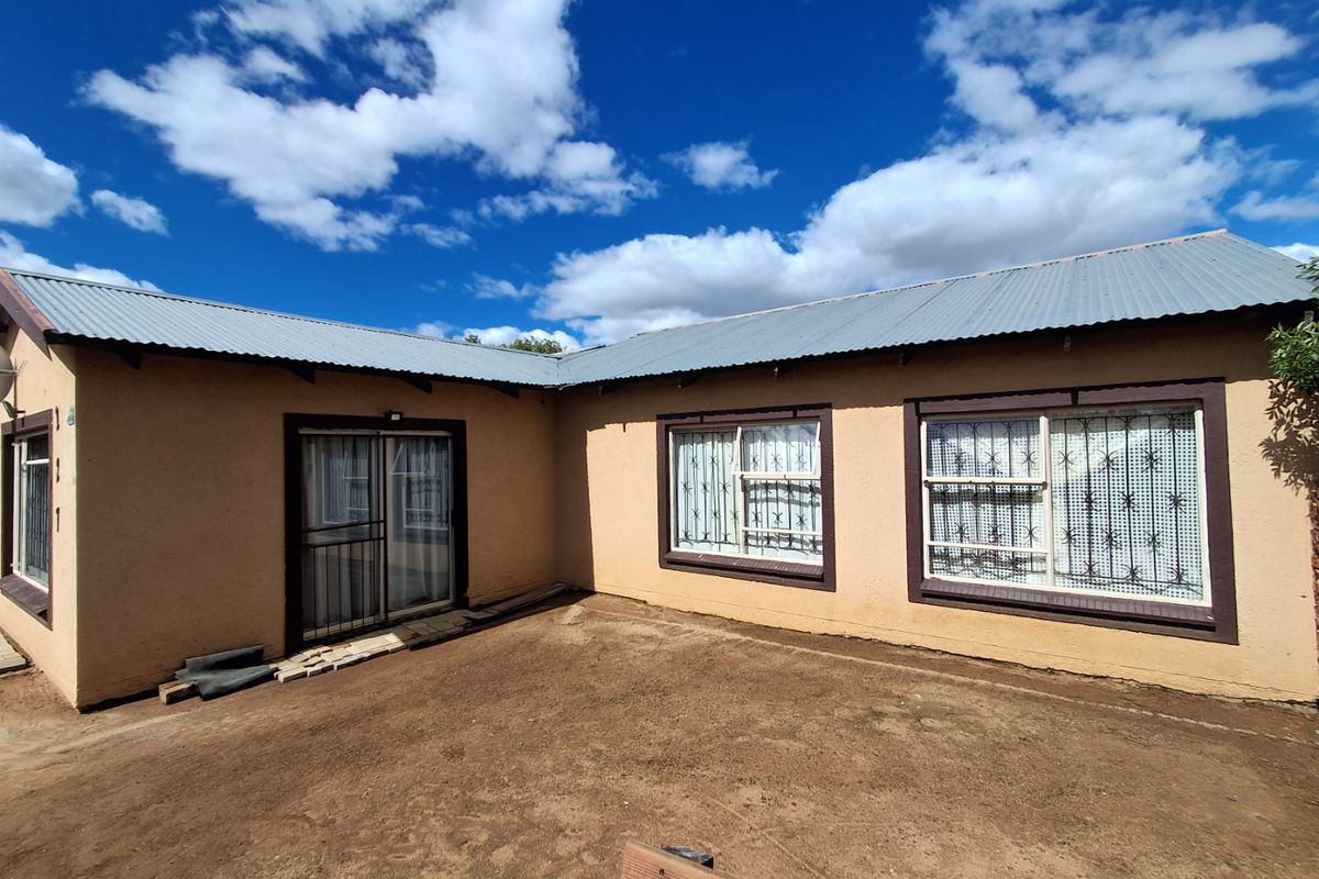 Rear exterior view of the house featuring plastered walls, corrugated metal roofing, and security-fitted windows and sliding door.