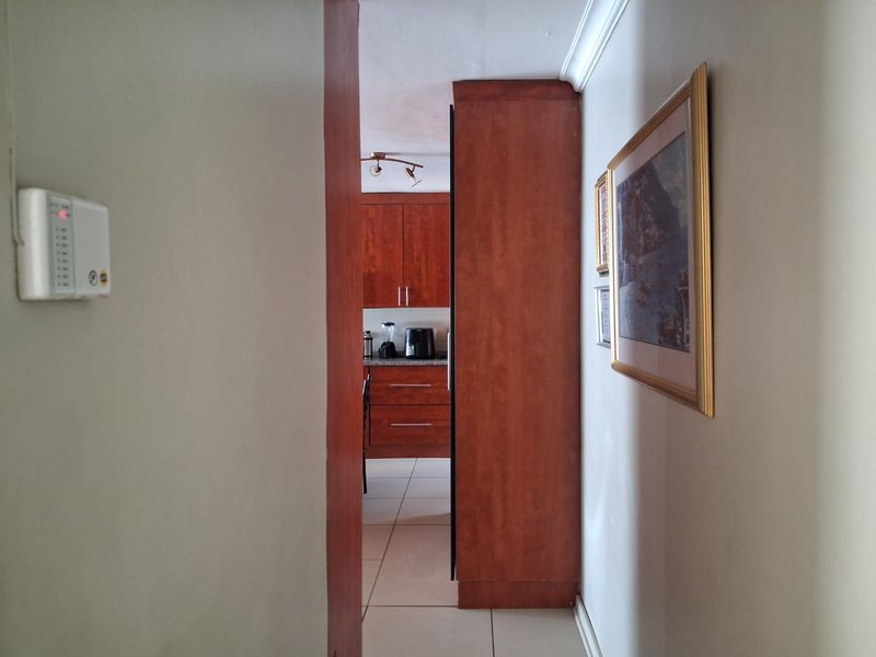 A view through a hallway towards a kitchen area featuring built-in wooden cabinetry and tiled flooring.