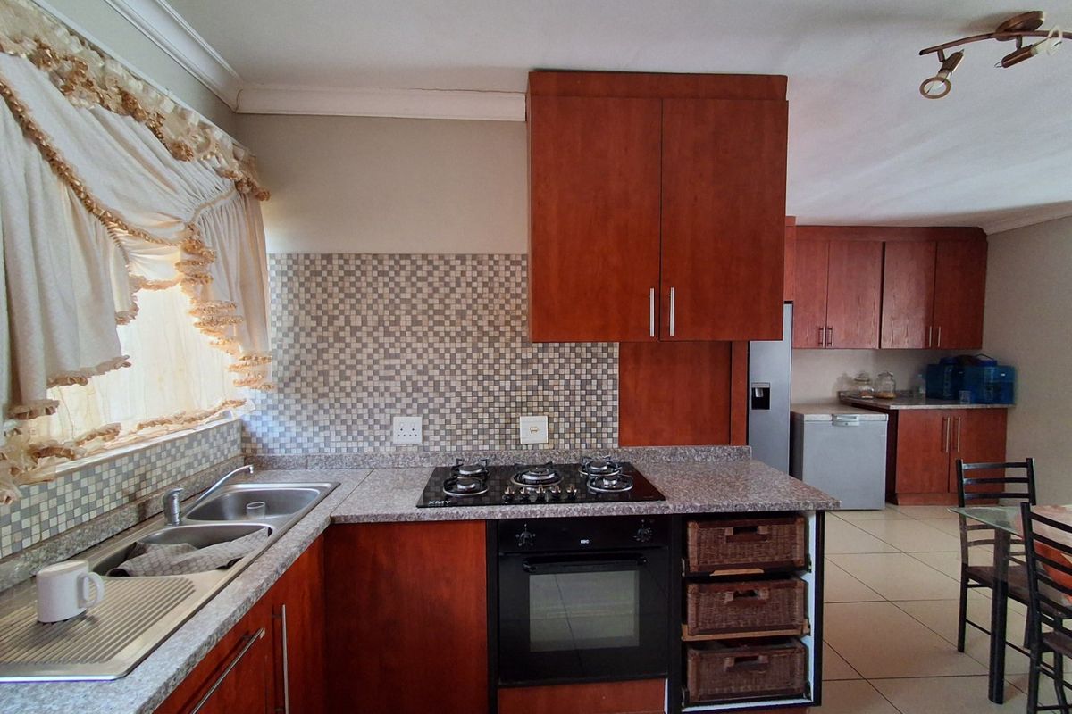 Functional kitchen featuring dark wood cabinetry, granite countertops, a gas hob, built-in oven, and a mosaic tile backsplash with tiled flooring throughout.
