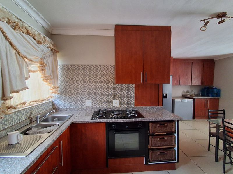 Functional kitchen featuring dark wood cabinetry, granite countertops, a gas hob, built-in oven, and a mosaic tile backsplash with tiled flooring throughout.