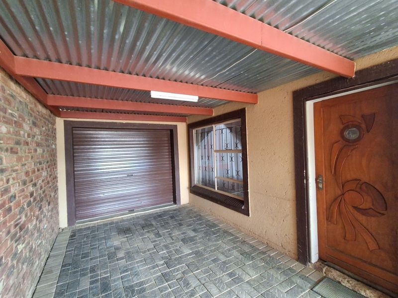 Covered entrance area featuring a paved driveway, roller shutter garage door, and a decorative carved wooden front door.